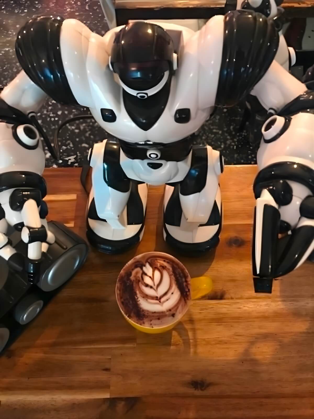 White robot toy beside a cup of coffee on a wooden table at The Robot Bun Factory